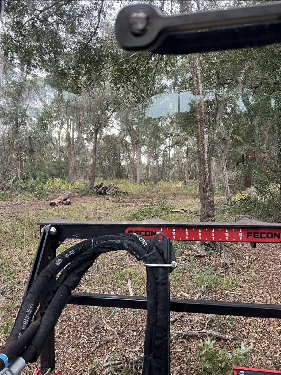 View from Fecon mulcher cab looking out at wooded lot with Fecon gauge bar visible in Florida