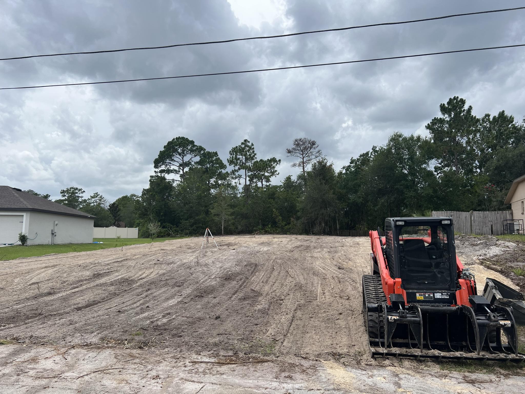 Kubota skid steer with grapple on cleared neighborhood lot with survey tripod in Deltona