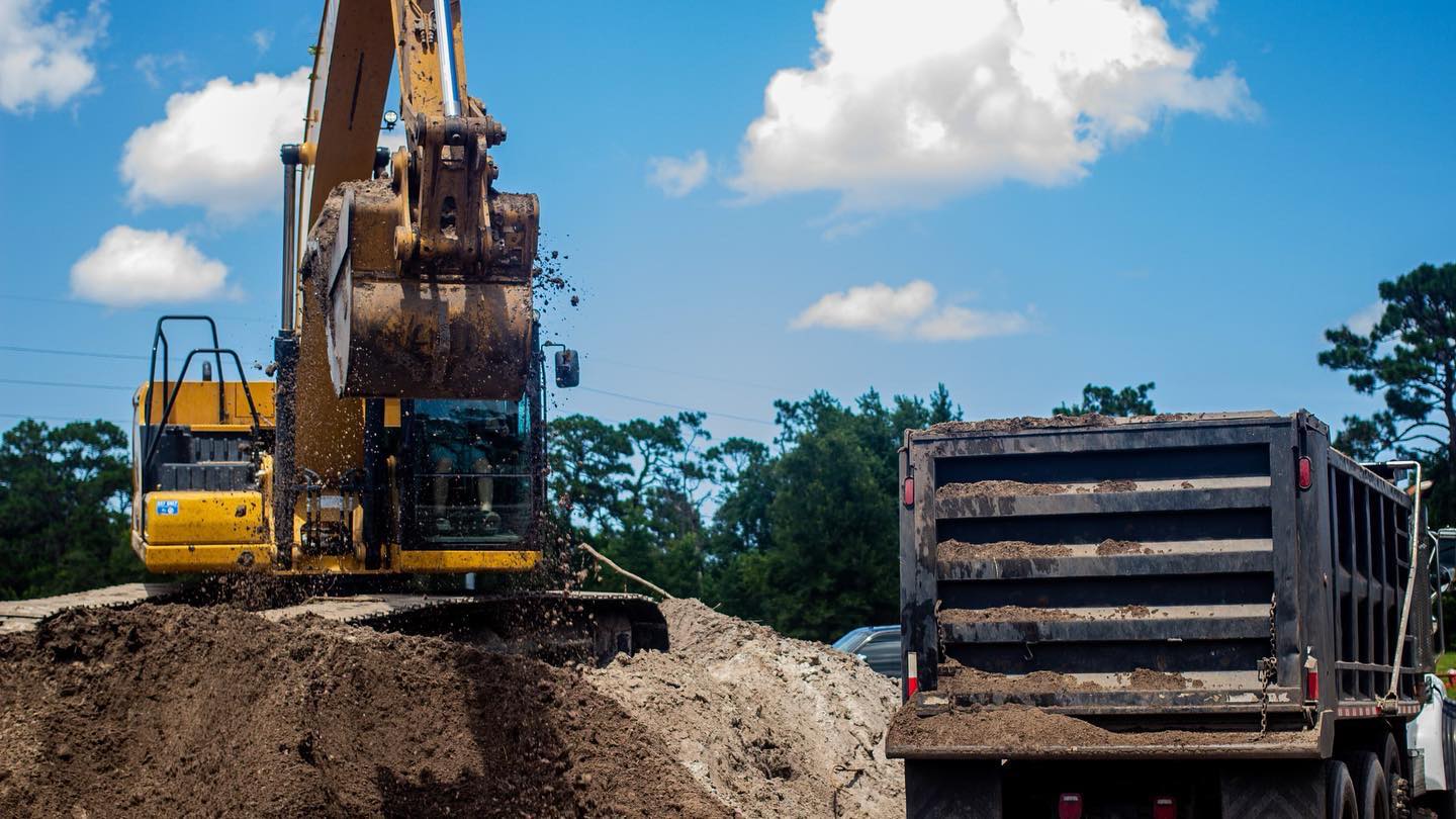 CAT excavator loading dirt into dump truck during pond excavation in Volusia County, FL