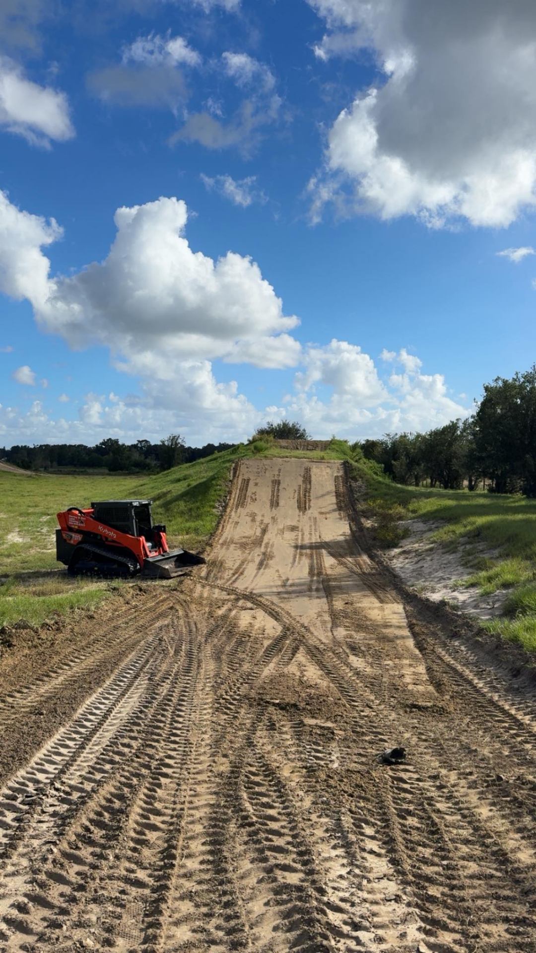 Kubota skid steer at base of large dirt jump during motocross track construction in Florida