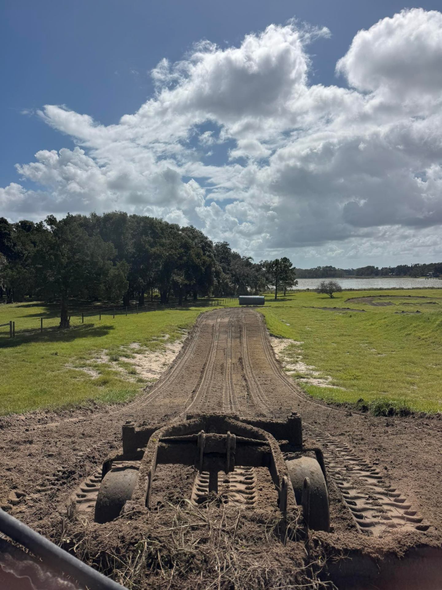 View from grader attachment smoothing motocross track straight with green field and oaks in Florida